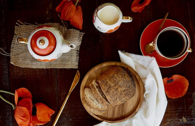 Bollo tradicional de semillas de amapola con taza de té y leche entre flores de amapola y platos con amapolas