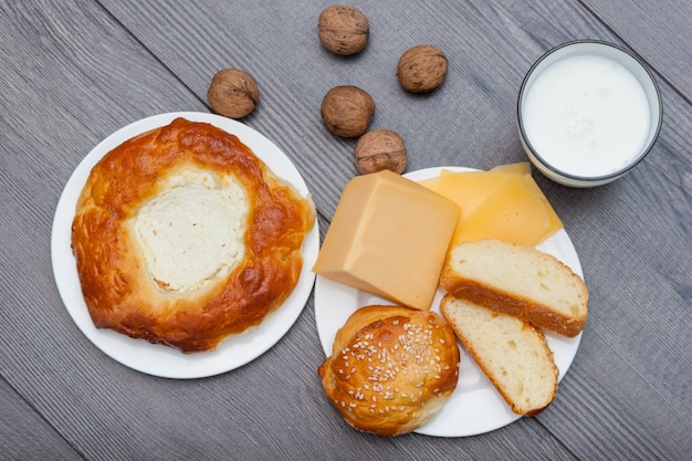 Bollos caseros frescos con sésamo y queso sobre fondo de madera con vaso de leche, manzana, nueces.