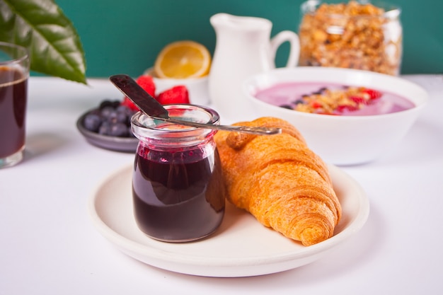 Bollos de cruasanes recién hechos, bayas, mermelada de grosella negra y un vaso de café. Concepto de desayuno.