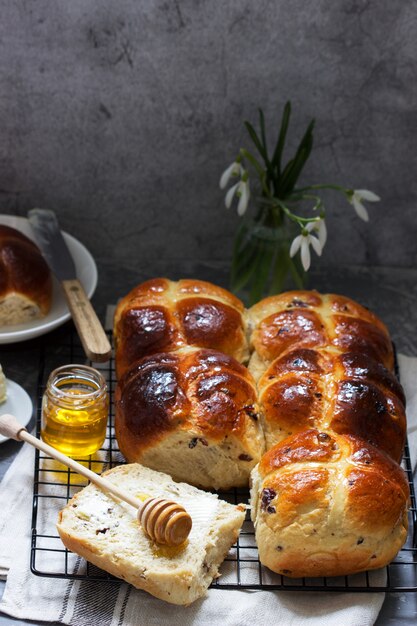 Bollos cruzados calientes tradicionales con miel y mantequilla sobre una superficie de hormigón