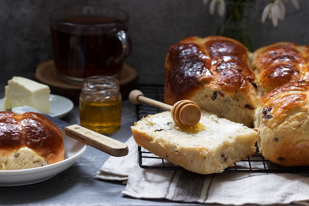 Bollos cruzados calientes tradicionales con miel y mantequilla sobre una superficie de hormigón