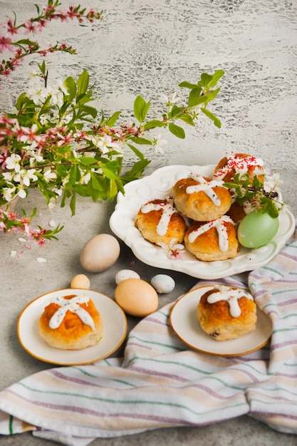 Bollos cruzados calientes tradicionales de Pascua caseros y huevos pintados sobre una superficie gris