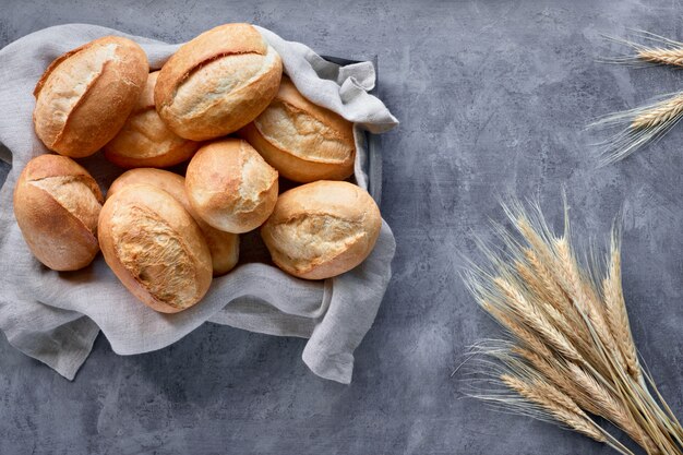 Bollos de pan en la cesta de madera rústica con espigas, vista superior en gris