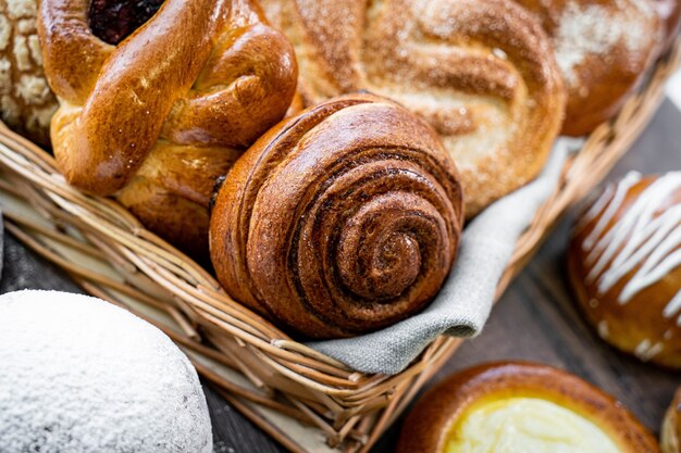 Bollos de pastelería fresca en la canasta en panadería de estilo rústico con trigo blanco sobre mesa de madera