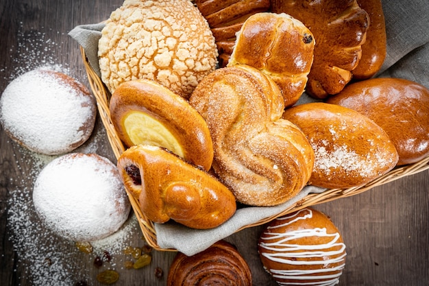 Bollos de pastelería fresca en la canasta en panadería de estilo rústico con trigo blanco sobre mesa de madera