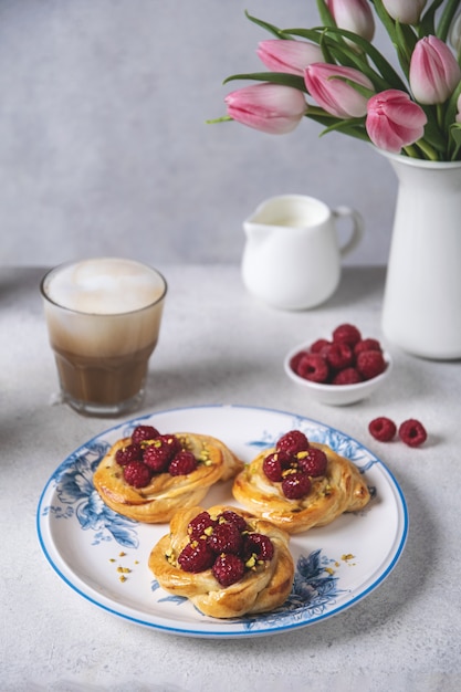 Bollos recién horneados con frambuesas y café capuchino en mesa blanca