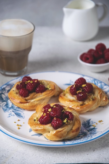 Bollos recién horneados con frambuesas y café capuchino en mesa blanca