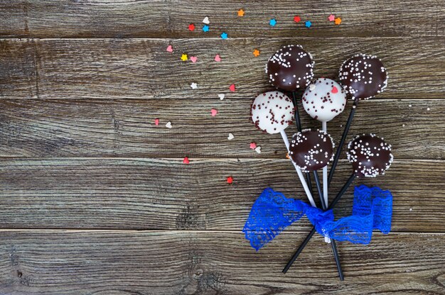 Bolo aparece. Doces doces em esmalte de chocolate branco e preto, no palito em um fundo de madeira.