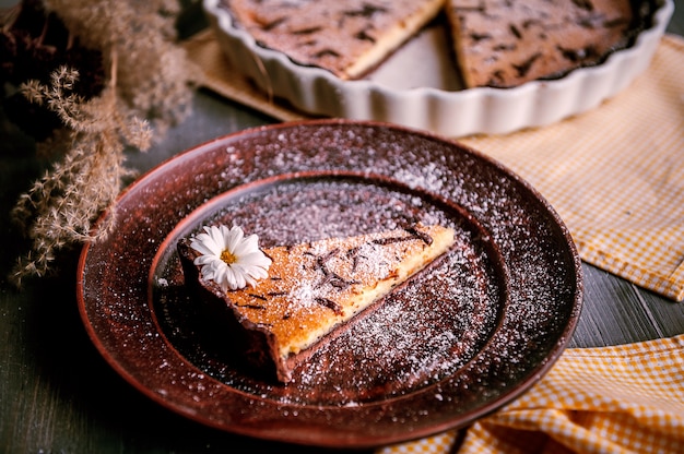 Bolo assado em forma de cerâmica polvilhada com fatias de chocolate em uma mesa de madeira.