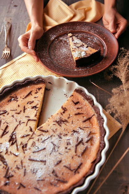 Bolo assado em forma de cerâmica polvilhada com fatias de chocolate em uma mesa de madeira.