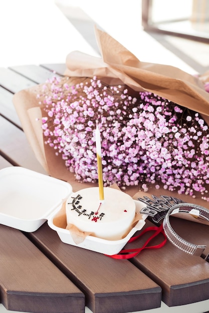 Bolo Bento com uma vela com um buquê de gypsophila rosa em uma mesa de madeira em um café