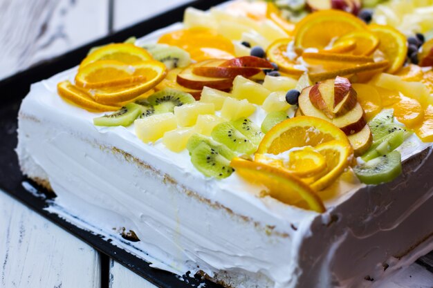 Bolo branco com pedaços de fruta. fatias de kiwi e laranja. bolo caro feito sob medida. sobremesa festiva em um restaurante.