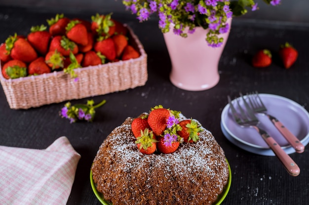 Bolo caseiro com morangos frescas, placa, vaso com flores.