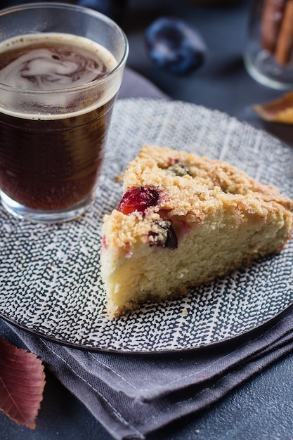 Bolo caseiro da ameixa e vidro rústicos do café no fundo concreto escuro. Torta de frutas doces.