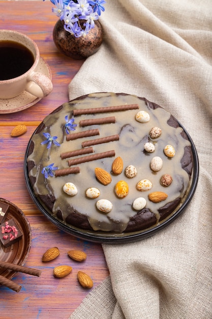 Bolo caseiro de brownie de chocolate com creme de caramelo e amêndoas com café em um fundo de madeira colorido e têxteis de linho.