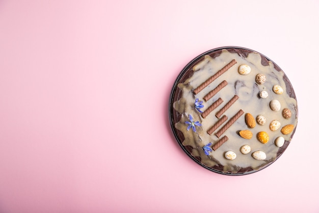 Bolo caseiro de brownie de chocolate com creme de caramelo e amêndoas em um fundo rosa pastel.