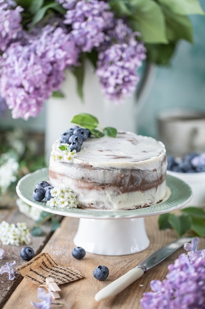 Bolo caseiro de cereja com creme mascarpone sobre um fundo claro e um buquê de flores de cerejeira e lilases.