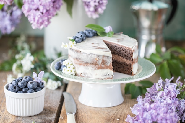 Bolo caseiro de cereja com creme mascarpone sobre um fundo claro e um buquê de flores de cerejeira e lilases.