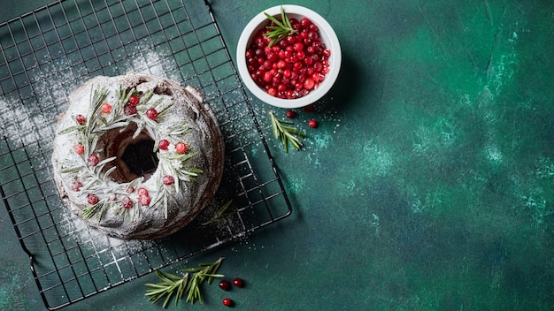 Bolo caseiro de chocolate amargo feito em casa, decorado com açúcar de confeiteiro e cranberries frescas em uma grade de metal em fundo verde escuro