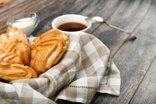 Bolo choux com café em um de madeira. em uma cesta em uma toalha quadriculada. . chique com queijo cottage. bolos de creme pequeno na tigela de vime na madeira