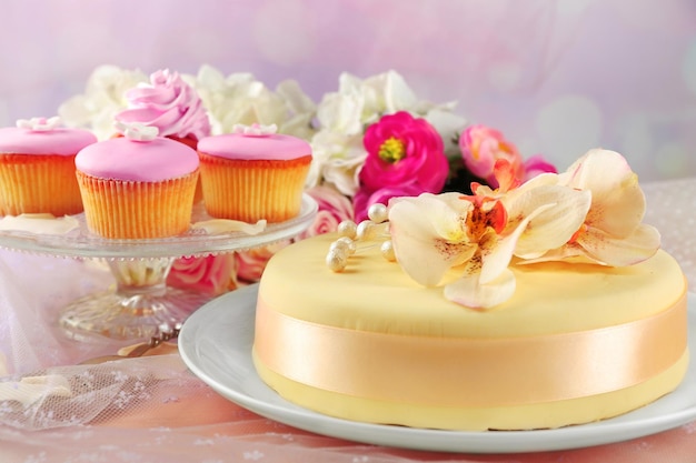 Bolo com flores de pasta de açúcar e cupcakes na luz de fundo