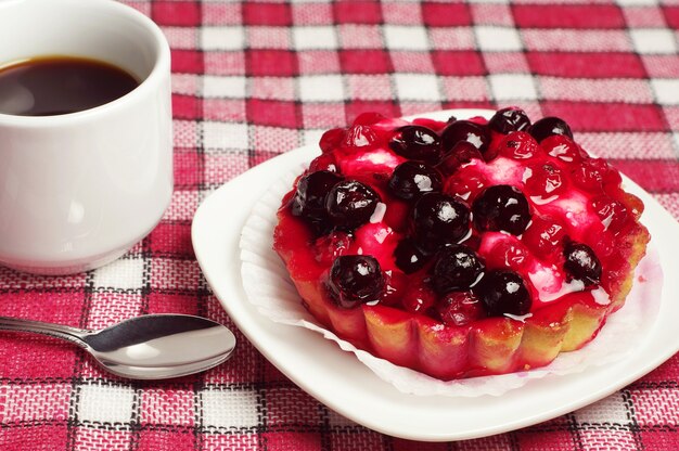 Bolo com frutas no prato e xícara de café na mesa, toalha de mesa vermelha