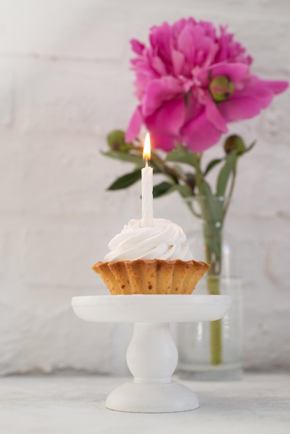 Bolo com uma vela em um carrinho de bolo em um fundo de flores e uma parede de tijolos brancos