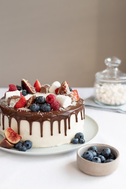 Bolo de aniversário coberto com frutas vermelhas e gotas de chocolate na toalha de mesa branca Conceito moderno de padaria