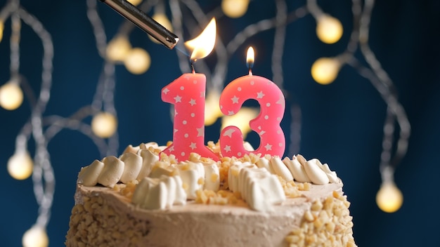 Bolo de aniversário com 13 velas rosa número em fundo azul incendiado pelo isqueiro. Vista de perto