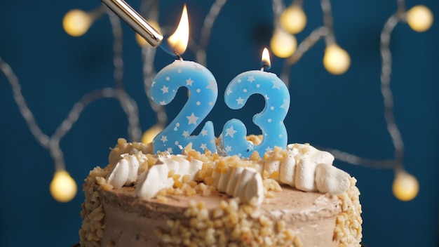 Bolo de aniversário com 23 velas número no fundo azul incendiado pelo isqueiro. Fechar-se