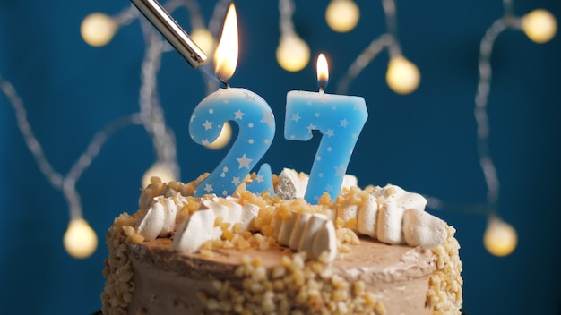 Bolo de aniversário com 27 velas número no fundo azul incendiado pelo isqueiro. Fechar-se