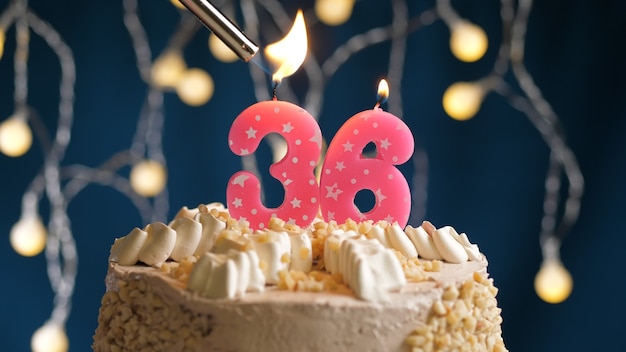 Bolo de aniversário com 36 velas rosa número sobre fundo azul incendiado pelo isqueiro. Vista de perto