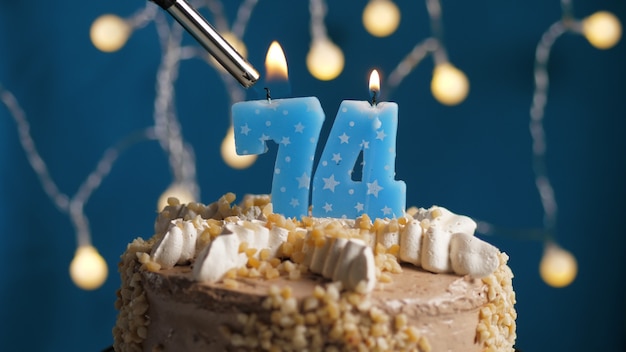 Bolo de aniversário com 74 velas número no fundo azul incendiado pelo isqueiro. Fechar-se