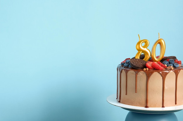 Bolo de aniversário de chocolate com biscoitos de bagas e número oitenta velas douradas no espaço de cópia de fundo de parede azul