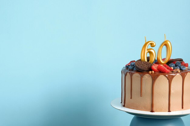 Bolo de aniversário de chocolate com biscoitos de bagas e número sessenta velas douradas no espaço de cópia de fundo de parede azul