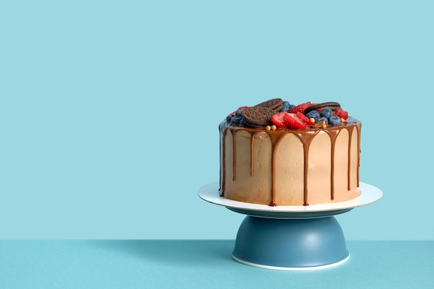 Bolo de aniversário de chocolate com frutas e biscoitos no espaço de cópia de fundo de mesa de parede azul