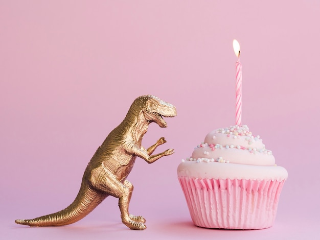 Foto bolo de aniversário e dinossauro engraçado em fundo rosa