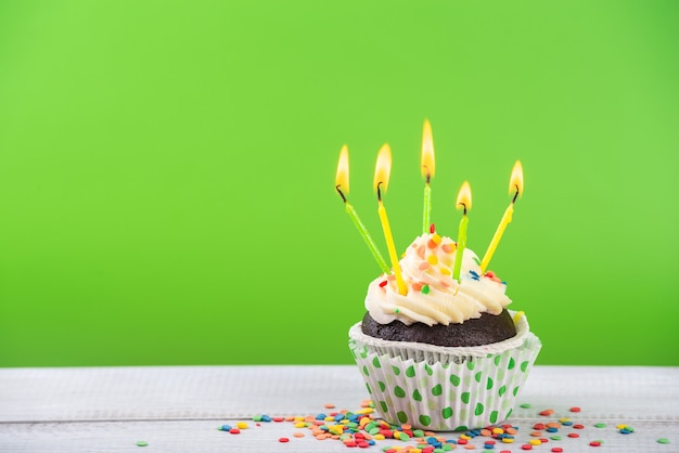 Bolo de aniversário em verde com velas multicoloridas.