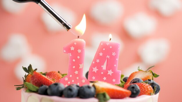 Bolo de aniversário número 14 vela rosa no lindo bolo com bagas e isqueiro com fogo contra o fundo de nuvens brancas e céu rosa Vista aproximada