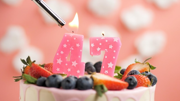 Bolo de aniversário número 47 vela rosa no lindo bolo com bagas e isqueiro com fogo contra o fundo de nuvens brancas e céu rosa Vista aproximada