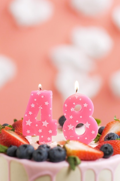 Bolo de aniversário número 48 Linda vela rosa no bolo em fundo rosa com nuvens brancas Closeup e vista vertical