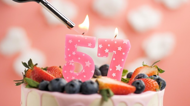 Bolo de aniversário número 57 vela rosa no lindo bolo com bagas e isqueiro com fogo contra o fundo de nuvens brancas e céu rosa Vista aproximada