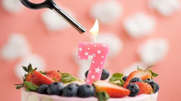 Bolo de aniversário número 7 vela rosa no lindo bolo com bagas e isqueiro com fogo contra o fundo de nuvens brancas e céu rosa Vista aproximada