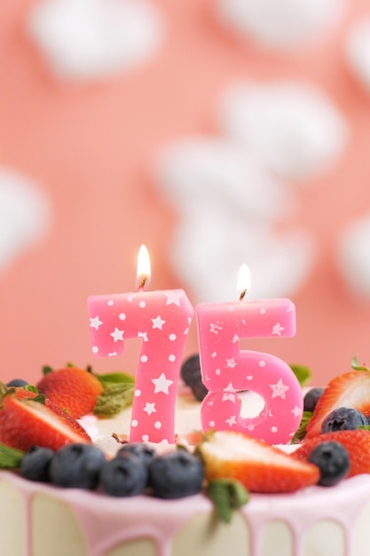 Bolo de aniversário número 75 Linda vela rosa no bolo em fundo rosa com nuvens brancas Closeup e vista vertical