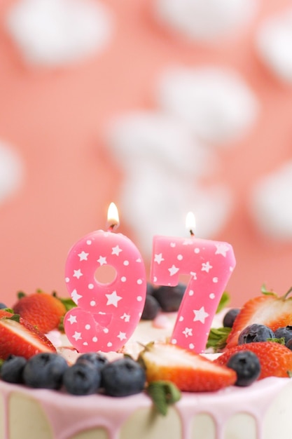 Bolo de aniversário número 97 Linda vela rosa no bolo em fundo rosa com nuvens brancas Closeup e vista vertical