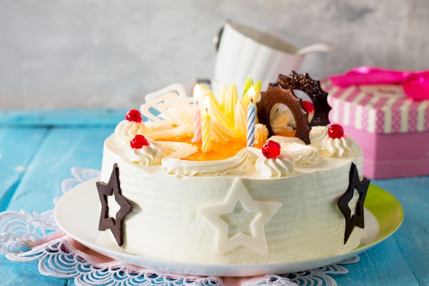 Bolo de aniversário pão-de-ló com chantilly e velas coloridas sobre fundo azul