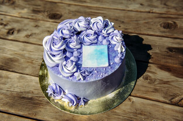 Bolo de aniversário roxo com flores creme e adesivo decorativo em fundo de madeira