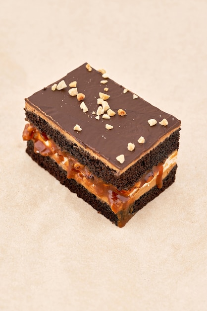 Bolo de biscoito escuro com uma camada de creme e fondant de chocolate, polvilhado com nozes raladas, moldura vertical