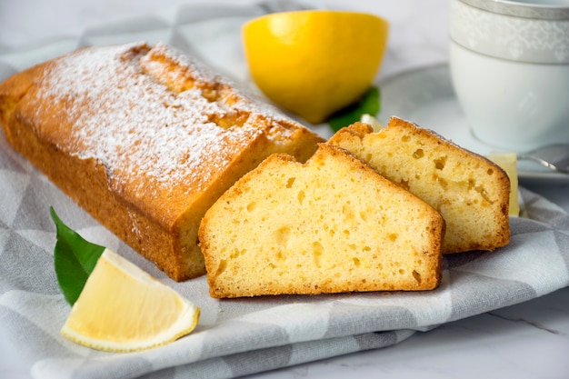 Bolo de bolo de limão sem glúten, pedaços de limão e xícara no pano de prato na mesa de mármore