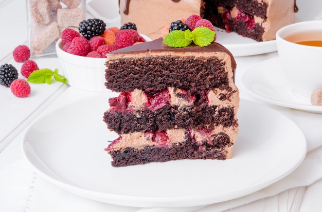 Bolo de camada de chocolate com recheio de cereja e frutas frescas por cima em um prato branco.